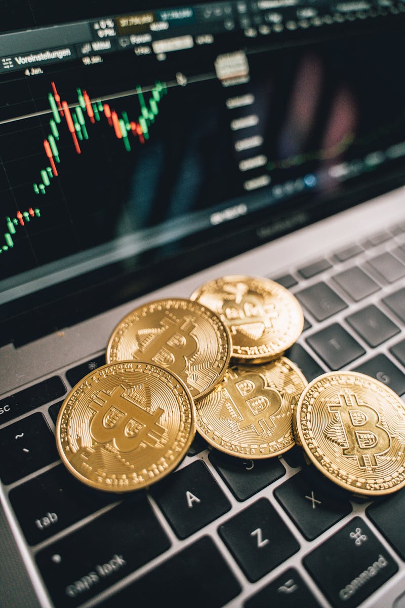 Close-up of gold Bitcoin coins on a laptop keyboard with a stock chart, symbolizing cryptocurrency market analysis.